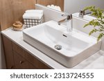 detail in interior of bathroom, modern ceramic wash basin with chrome water faucet, clean towels in metal basket and wooden massage brush