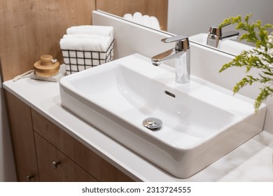 detail in interior of bathroom, modern ceramic wash basin with chrome water faucet, clean towels in metal basket and wooden massage brush