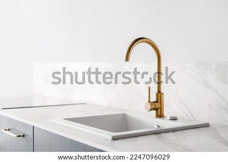 detail in interior at luxury kitchen with golden shiny faucet and rectangular sink built in marble countertop on wall background with copy space