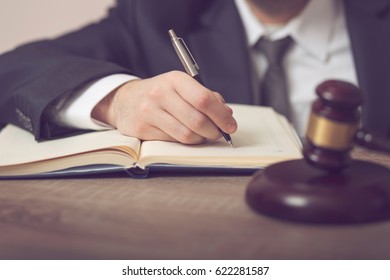 Detail Of A Judge Sitting At His Desk, Studying New Laws And Legislation And Taking Notes. Selective Focus