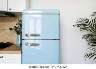 Detail in kitchen interior, blue refrigerator with stainless steel handles in retro style near cabinet on white wall background. Fridge for storage food products at home. Household appliances concept