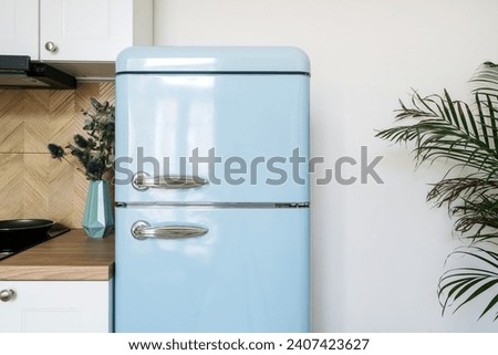 Detail in kitchen interior, blue refrigerator with stainless steel handles in retro style near cabinet on white wall background. Fridge for storage food products at home. Household appliances concept