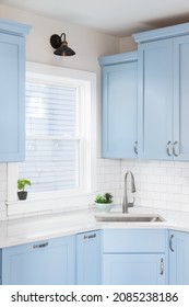 Detail Of A Kitchen With Light Blue Cabinets, White Granite Countertop, Subway Tile Backsplash, And A Light Hanging Above A Window.