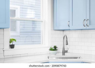 Detail Of A Kitchen With Light Blue Cabinets, White Granite Countertop, Subway Tile Backsplash, And A Light Hanging Above A Window.