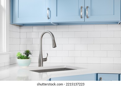 Detalle de una cocina con armarios de color azul claro, encimera de granito blanco, resplandor de baldosas del metro y una luz que cuelga sobre una ventana.