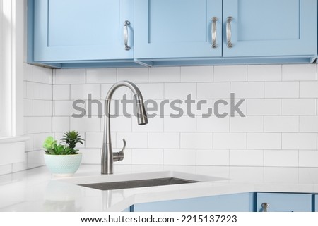 Detail of a kitchen with light blue cabinets, white granite countertop, subway tile backsplash, and a light hanging above a window.