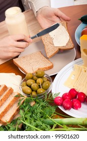 Detail Of Kitchen Table And Female Hands Spreading Mayonnaise On Sandwiches.