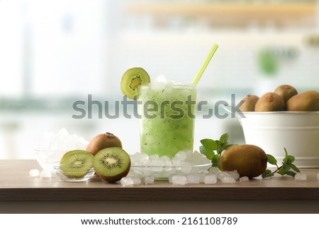 Detail of kiwi soft drink with a lot of ice on a wooden kitchen bench with fruit and a bowl with ice around it. Front view. Horizontal composition.