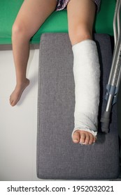 Detail left leg or in white plaster placed on a gray sofa or stool.Broken leg in plaster. The boy has a broken ankle.