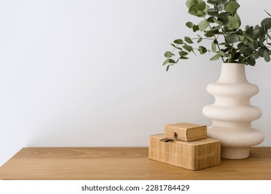 detail in living room interior, modern vase with eucalyptus branch and small bamboo jewelry box on wooden table on white wall background with copy space - Shutterstock ID 2281784429