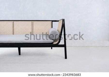 Detail of long sofa made of black painted wood with rattan backrest and foam seat complete with pillows