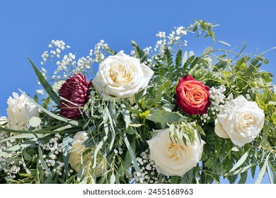 Detail of a lush garland also known as flower leis or floral wreath featuring large white roses, baby-breath and greenery, set against the blue sky, common bridal detail used for the wedding ceremony - Powered by Shutterstock