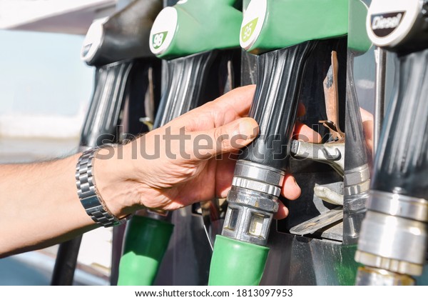 Detail of a male\
hand grasping a fueling nozzle among several with different octane\
diesel and gas for cars