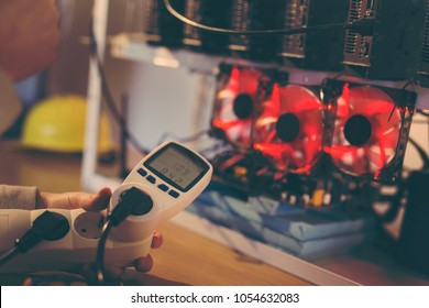 Detail of male hand holding a wattmeter measuring cryptocurrency mining rig energy consumption. Selective focus on the wattmeter - Shutterstock ID 1054632083