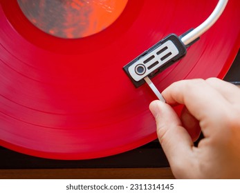Detail of a male hand placing the needle on the track of a red vinyl record. Vintage turntable - Shutterstock ID 2311314145