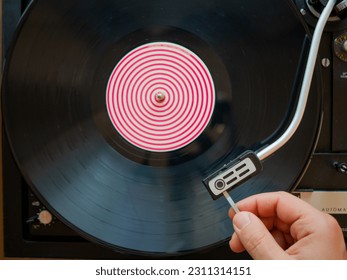 Detail of a male hand placing the needle on the track of a black vinyl record. Vintage turntable - Shutterstock ID 2311314151