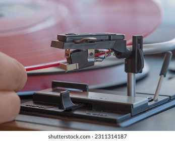 Detail of a male hand placing a red vinyl record on a vintage turntable - Shutterstock ID 2311314187