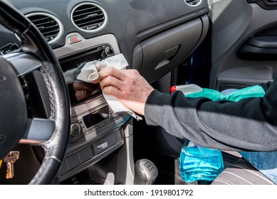 Detail Of A Man's Hand Wearing A Green Rubber Glove Cleaning The Screen On The Dashboard Of A Car With A Paper Towel. He Is Holding A Spray Bottle With A Blue Liquid In The Other Hand. Car Wash Worker