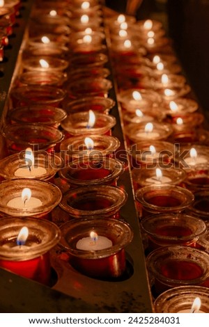 Detail of a metal candle stand in a Catholic cathedral. Small devotional lighted candles in small jars represent the petitions of the parishioners. Candles placed on a special candle holder. Vertical.