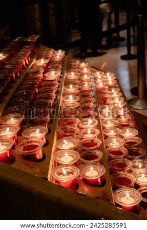 Detail of a metal candle stand in a Catholic cathedral. Small devotional lighted candles in small jars represent the petitions of the parishioners. Candles placed on a special candle holder. Vertical.