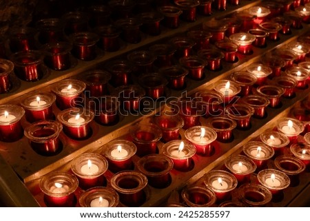 Detail of a metal candle stand in a Catholic cathedral. Small devotional lighted candles in small jars represent the petitions of the parishioners. Candles placed on a special candle holder. 