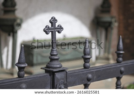 Detail of a metal fence with a cross and pointed elements in the cemetery area.