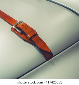 A detail of metallic grey car hood element with leather strap.
