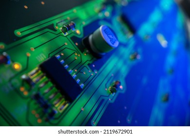 Detail of a microprocessor, resistors and capacitors soldered to a green glowing PCB printed circuit board with various connections and contacts