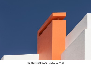 Detail of a modern rectangular building with straight white walls and an orange chimney against a blue sky, creating a geometric composition. Strong aesthetic appeal. Classic Blue. Abstract.