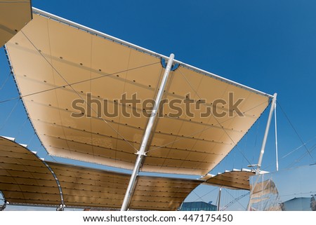 Detail of a modern tensile structure, membrane fabric roof with poles and steel cables, on a blue clear sky
