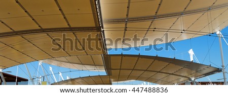 Detail of a modern tensile structure, membrane fabric roof with poles and steel cables, on a blue clear sky

