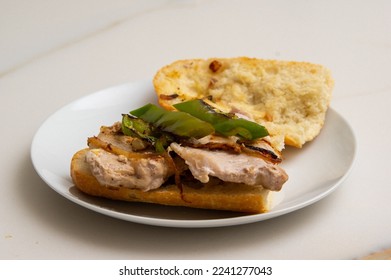 detail of a montadito de lomo: stale bread sandwich with a grilled pork loin steak with a fried green pepper and a little onion on a white plate on a white marble table