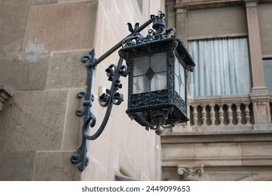 Detail of an old and ornate wrought iron lamp placed in the corner of a stone facade with an angled support. It is square and pretty - Powered by Shutterstock