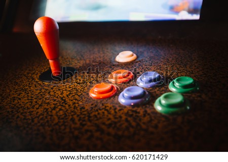 Detail on a joystick and button controls of a vintage arcade video game in a dark room with dark blue and yellow lights
