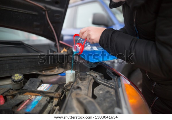 Detail\
on pouring anti-freeze liquid screen wash into dirty car from blue\
and red anti-freeze water container, car\
concept