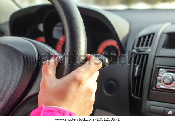 Detail on woman hand on leather car steering\
wheel while driving.