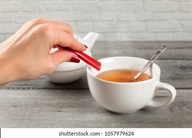 Detail On Woman Hand Pouring Sugar From Small Packet Into Cup Of Hot Tea.