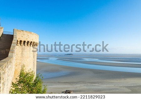 Detail of one of the defense tower of Mont Saint Michel, Normandy, France. On the right the coastline of atlantic ocean with sand and water during low tide.