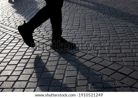 Detail of people rushing over the pavement at a train station during rush hour with sun coming from the side and long shadows
