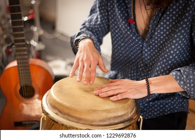Detail of a percussionist hands while playing congas instrument on a rehearsal studio with spanish guitar on the background. Membranophones percussion flamenco instruments concept. Musicology concept.