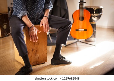 Detail of a percussionist male hands while playing flamenco drumbox on a rehearsal studio with drums and music stuff on the background with natural light. Flamenco instruments and musicology concept. 