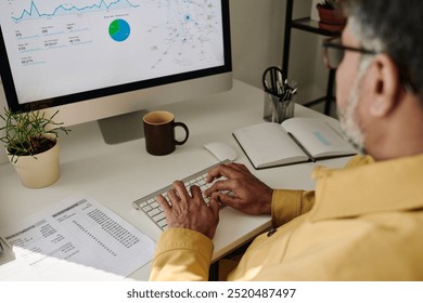 Detail of person analyzing financial data on desktop computer with charts and graphs visible on screen, working in bright and organized office environment, drinking coffee - Powered by Shutterstock