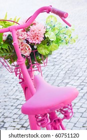 Detail of a pink painted bicycle with a basket with flowers and leaves