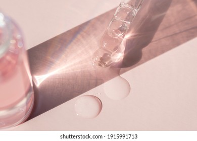 detail of a pipette with pouring serum and droplet with shadow on a pink background