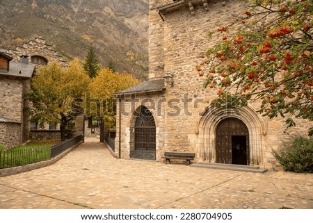 Detail plan of the stone portico of the church Santa María la Mayor next to a beautiful tree full of red fruits in the tourist village of Benasque, Huesca, Aragón.