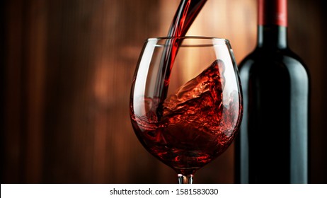 Detail of pouring red wine into glass, dark wooden background. Free space for text