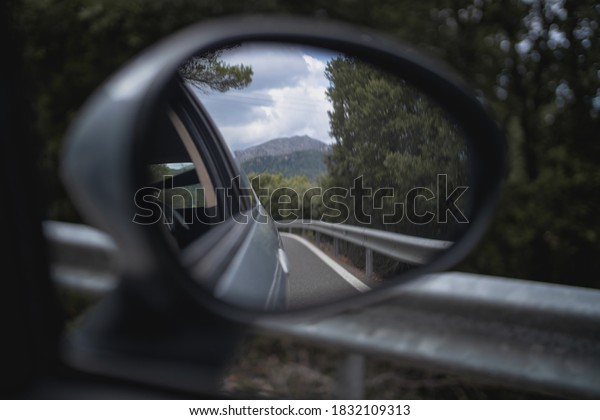Detail of the rear mirror of a car driving through a\
mountain road