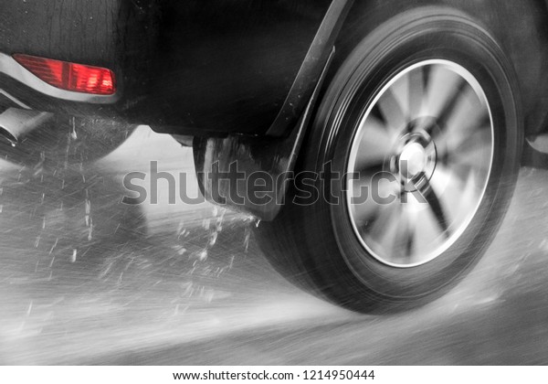 Detail of the rear wheel of\
a car driving in the rain on a wet road. Aquaplaning in road\
traffic.