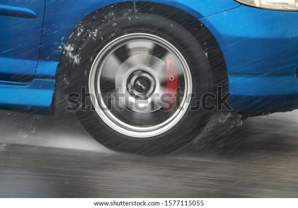 A Detail of the rear\
wheel of a car driving in the rain on a wet road. Aquaplaning in\
road traffic.