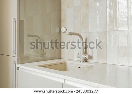 Detail of a rectangular kitchen sink with water tap against a tiled wall, stone table top, beidge monochrome design